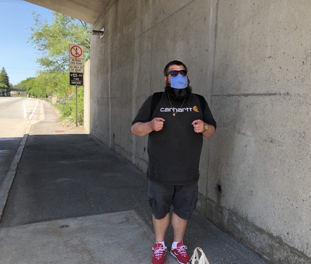 Photo of Marco Mancini, under a concrete underpass, with a cloth mask on and pointing his two index fingers at the camera