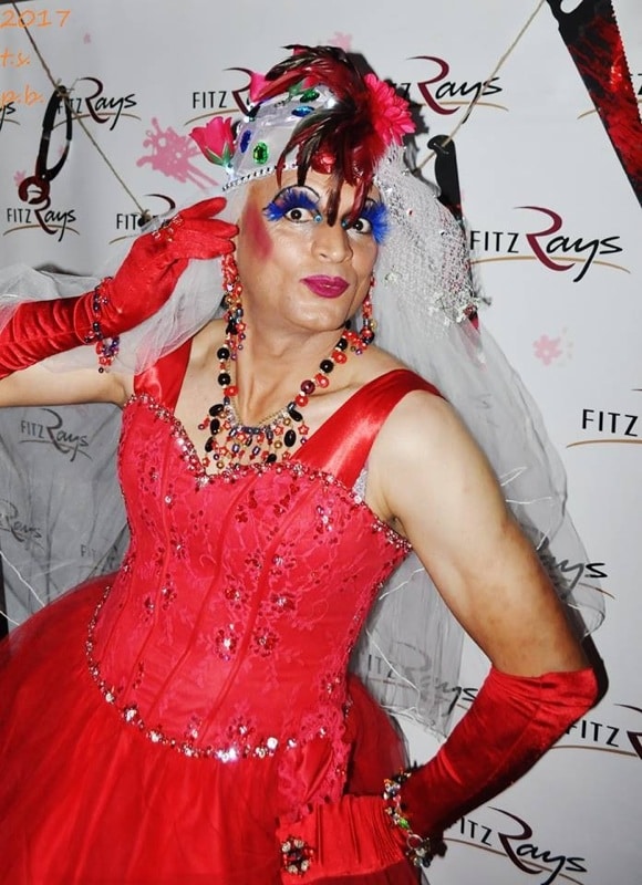 Katu Azzya as Mz. Affra-Tighty in a red dress, red gloves, a feathered headpiece and a veil
