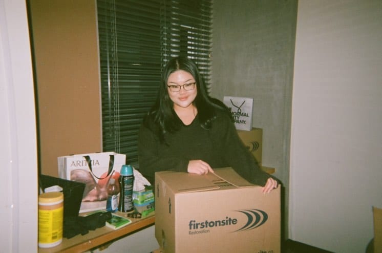 A picture of Sarah Law sitting with a few boxes and an Aritizia shopping bag.