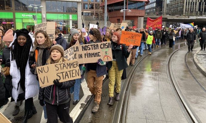greta thunberg and other people march, holding signs in swedish